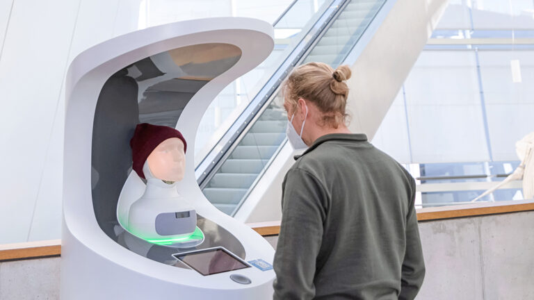 Besucher im OZEANEUM steht einem Service-Roboter mit menschlichen Gesichtszügen zugewandt.