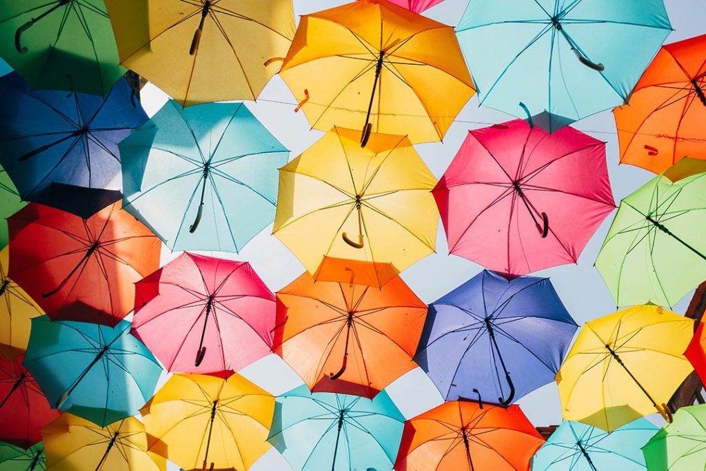 Bunte Regenschirme scheinen nebeneinander in der Luft zu schweben und bilden von unten gesehen Schutz vor der heißen Sonne oder weiteren Wetterereignissen.