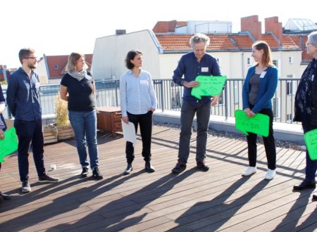 Eine Gruppe aus sieben Personen - meist Kulturschaffende aus Berlin - steht auf der sonnigen Dachterrasse der Technologiestiftung Berlin. Die Personen halten Schilder im Sprechblasenformat, auf denen eigene Wünsche und Bedarfe rund um das Thema Digitalisierung in der Kultur vermerkt sind.